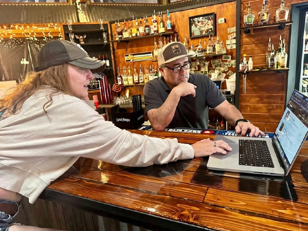 Marylou working through a website on a laptop with a bar owner at his counter
